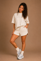 Woman wearing a beige outfit with shorts and a t-shirt on a brown background